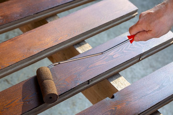 A man covers a wooden board with stain using a roller