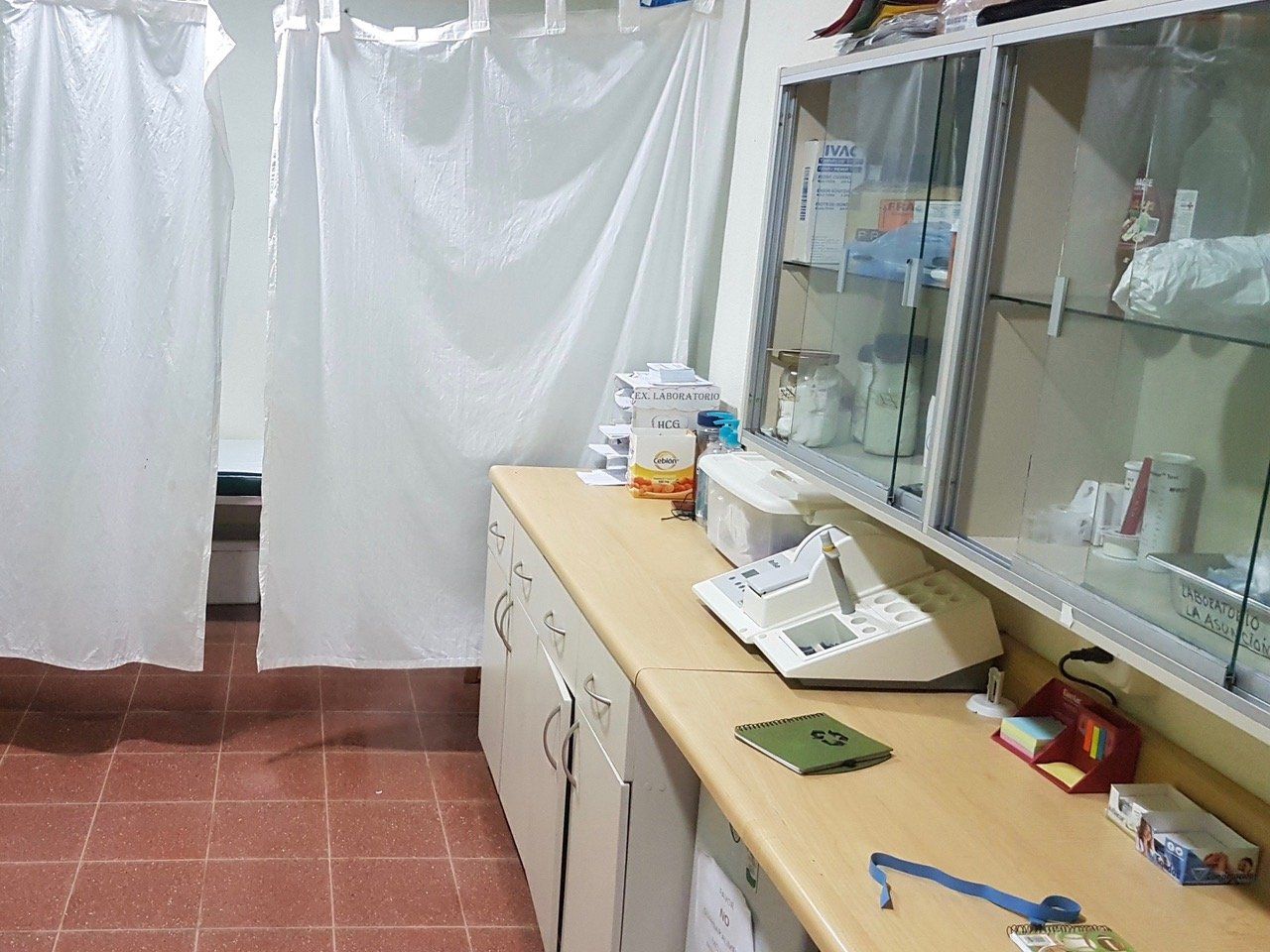 Ein Untersuchungsraum mit Vorhängen, Schränken, einer Theke und medizinischem Material.