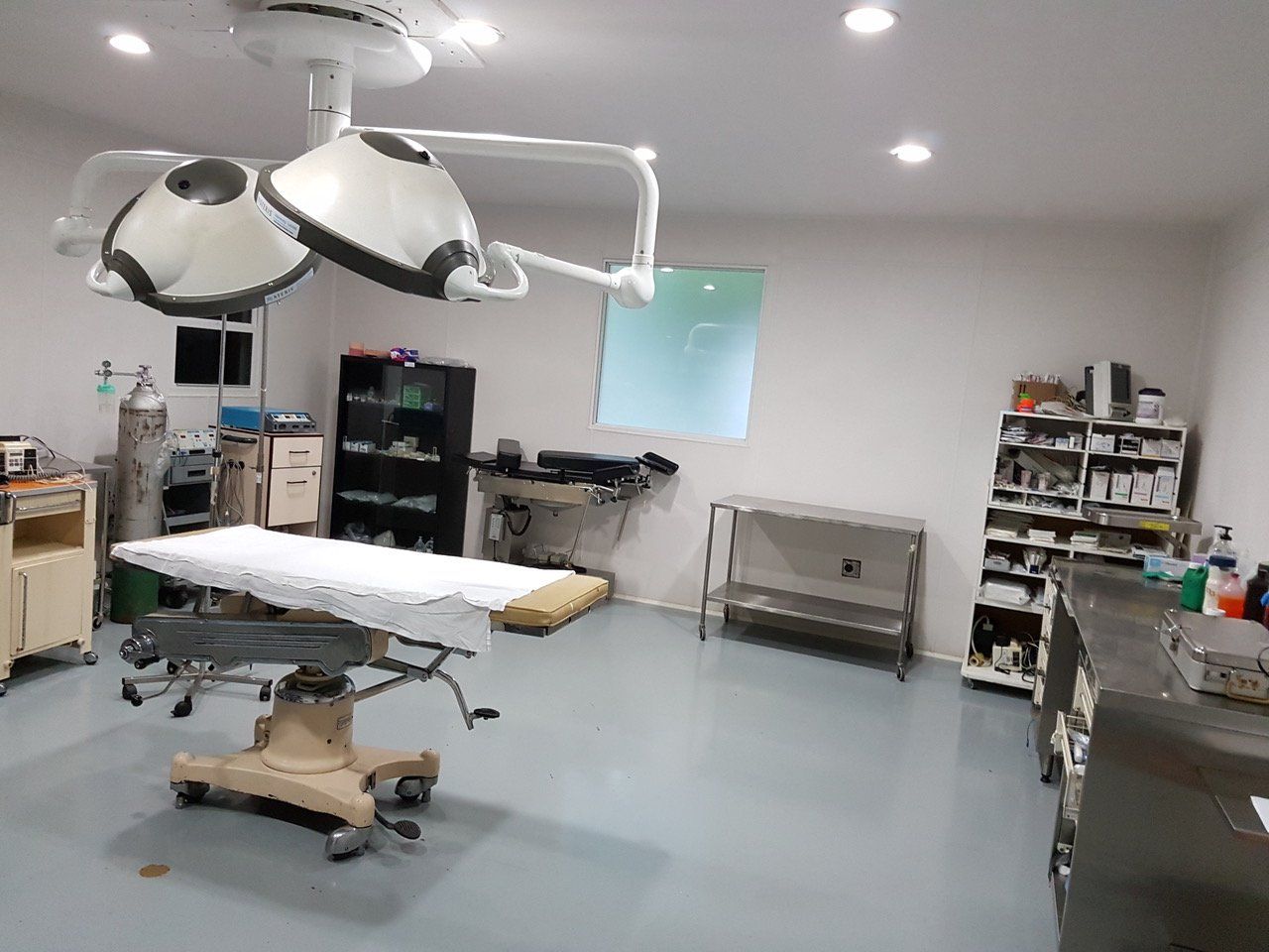 Ein Operationssaal mit OP-Leuchten über einem Tisch; Regale mit medizinischem Material.