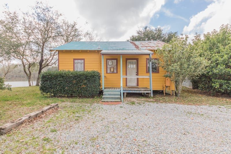 A small yellow house with a blue roof is sitting on top of a gravel lot.