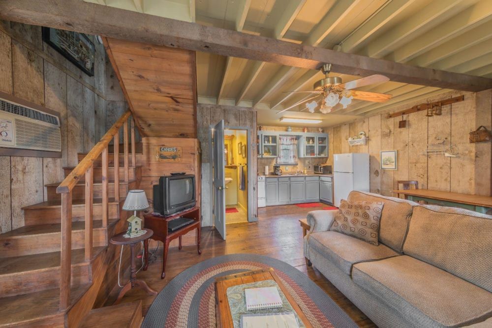A living room with a couch , television , stairs and a rug.