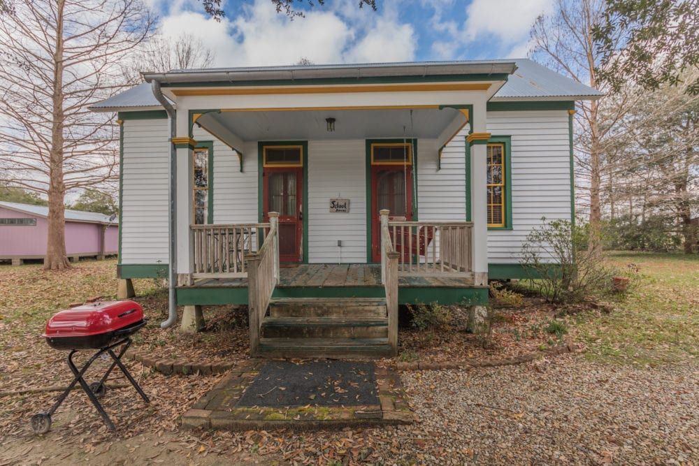 A small white house with a porch and stairs is for sale.