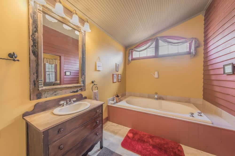 A bathroom with a tub , sink , mirror and window.