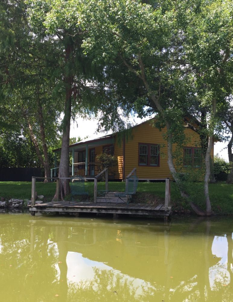 A yellow house is sitting on the shore of a lake surrounded by trees.