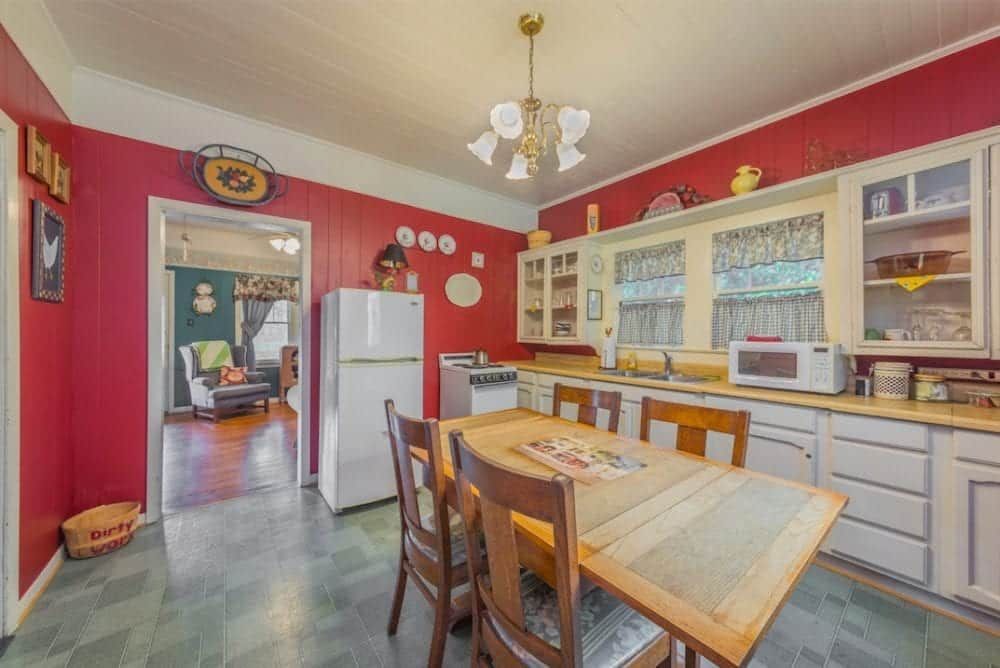 A kitchen with red walls , white cabinets , a table and chairs.