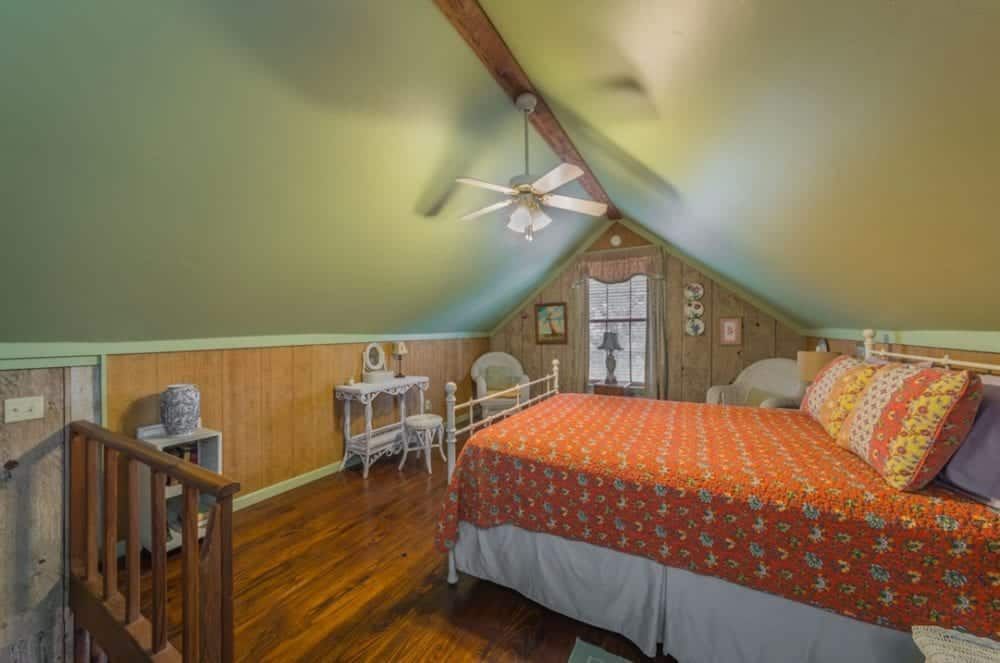 There is a bed in the attic with a ceiling fan.