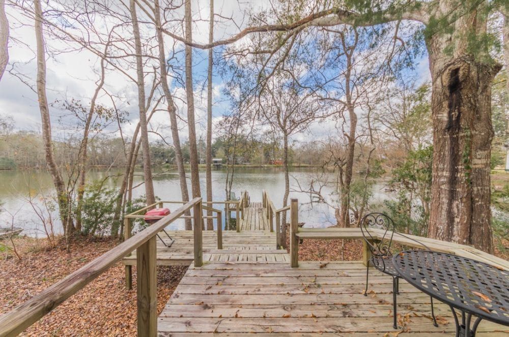A wooden deck with a table and chairs overlooking a lake surrounded by trees.