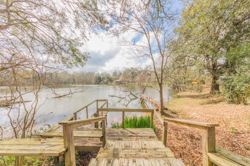 A wooden dock leading to a lake with trees in the background.