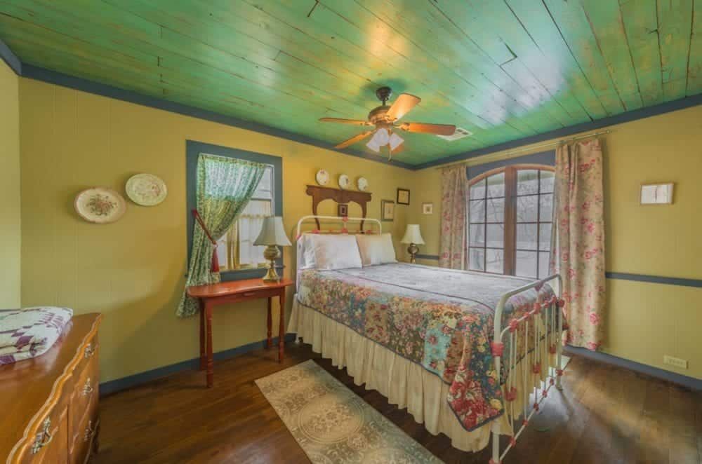 A bedroom with a bed , dresser , table and ceiling fan.