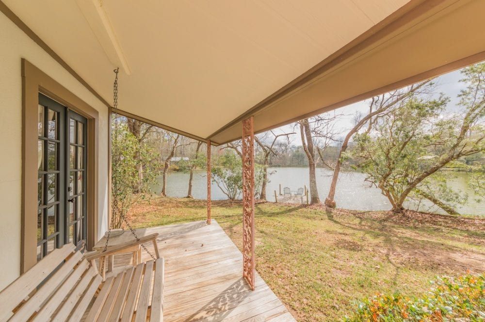 A porch with a swing and a view of a lake.