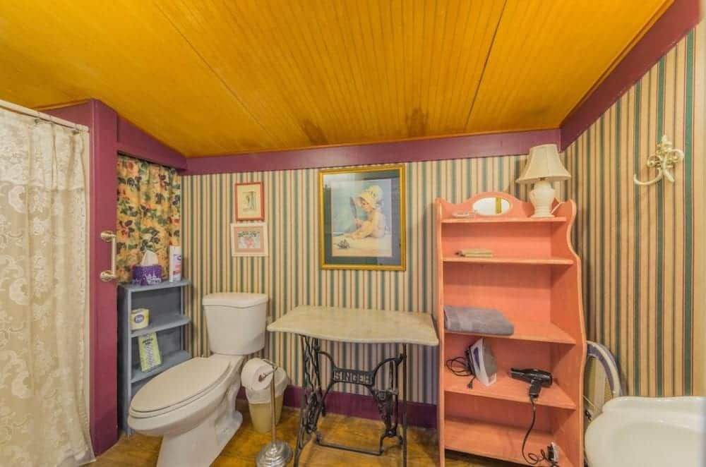 A bathroom with a toilet , sink , table and shelves.