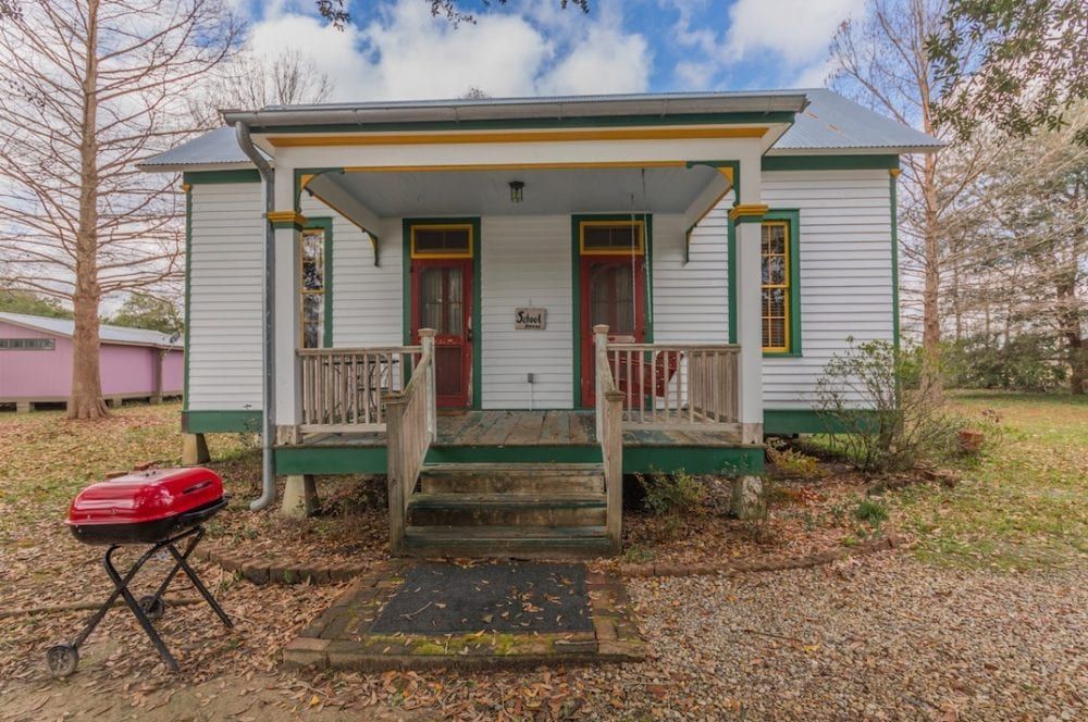 A small white house with a porch and a barbecue grill in front of it.