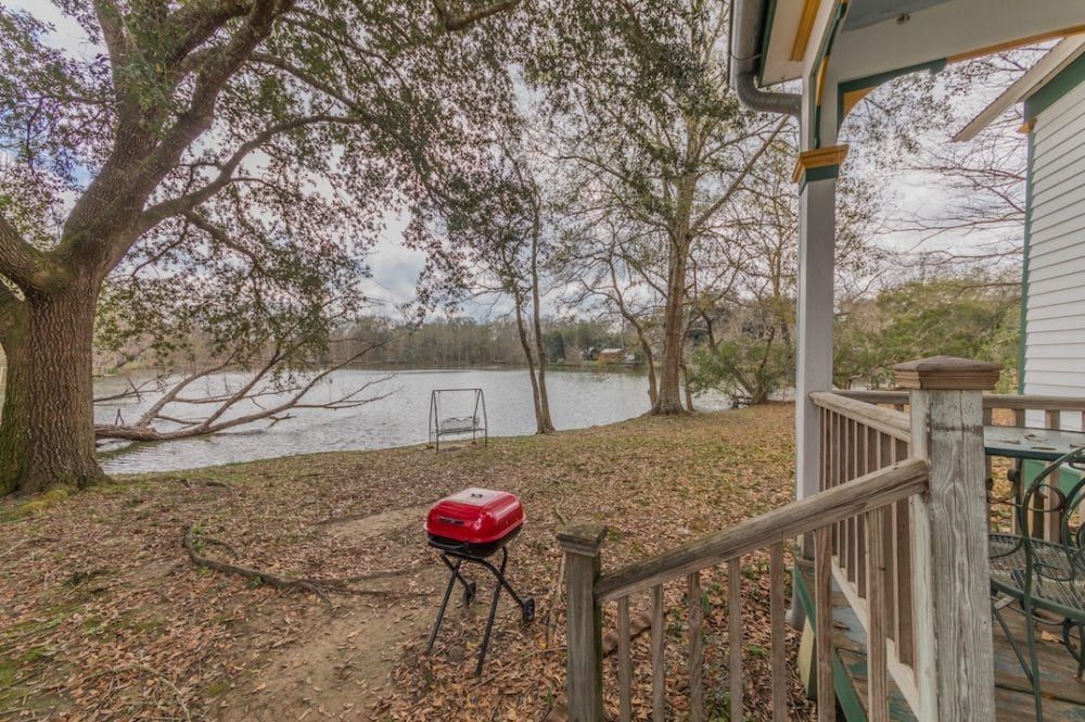 A red grill is sitting on a porch next to a lake.