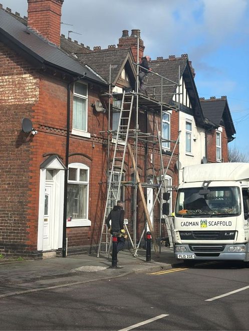 Ladders leaning against a brick row house as workers repair the roof on a residential street.