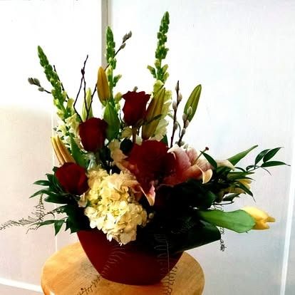 Floral arrangement in a red vase; includes red roses, lilies, and green foliage.