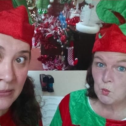 Two people in elf costumes making funny faces with Christmas decorations in the background.