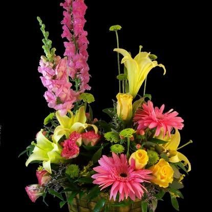 Floral arrangement with pink, yellow, and green flowers in a basket against a black background.