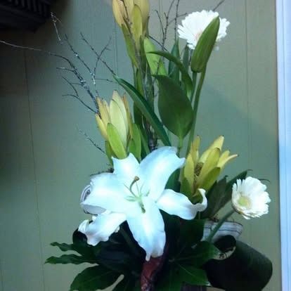 Floral arrangement with white lilies, daisies, and yellow flowers, against a light green wall.