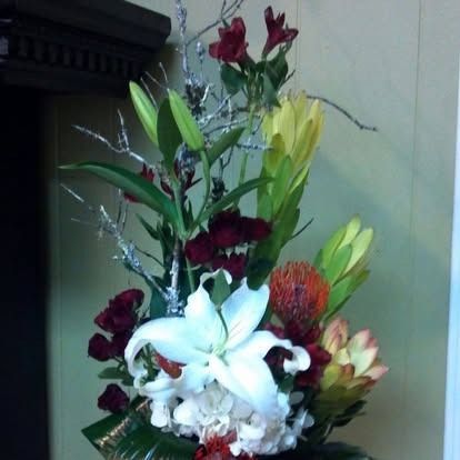 Floral arrangement with white lily, protea, and burgundy blooms.