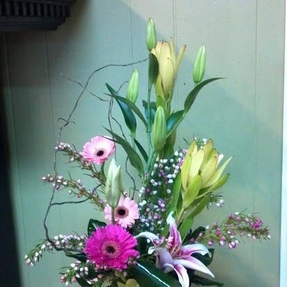 Floral arrangement with pink gerbera daisies, lilies, and greenery.
