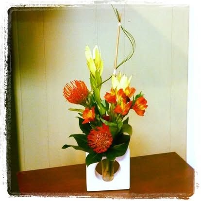 Floral arrangement in white vase: orange pincushion proteas, orange alstroemeria, and yellow gladioli.