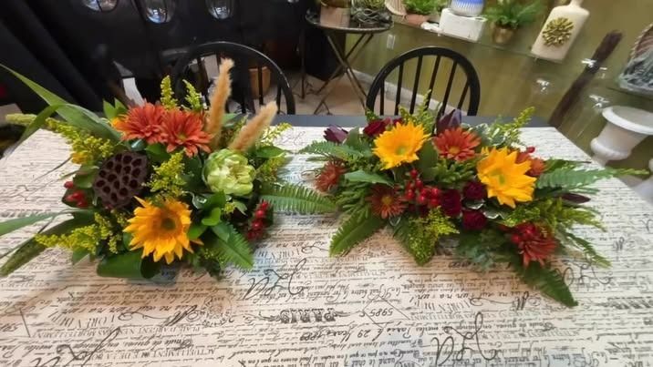 Two fall floral arrangements, orange and yellow blooms, on a table.