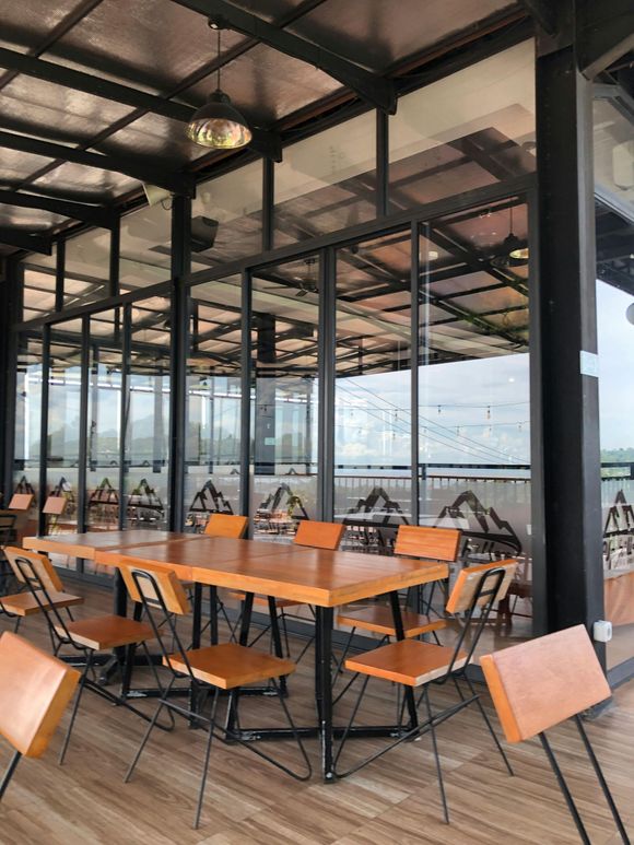 Restaurant patio with wooden tables and chairs, glass walls, and a view of mountains.
