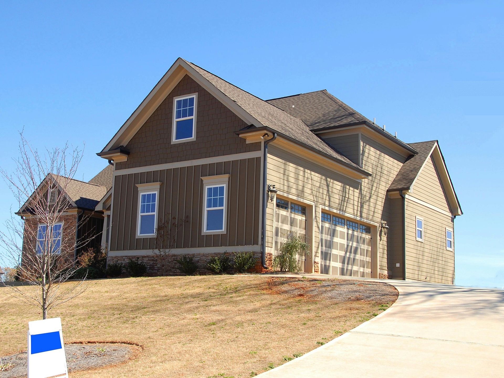 Two-story house with brown siding, two-car garage, and blue sky.