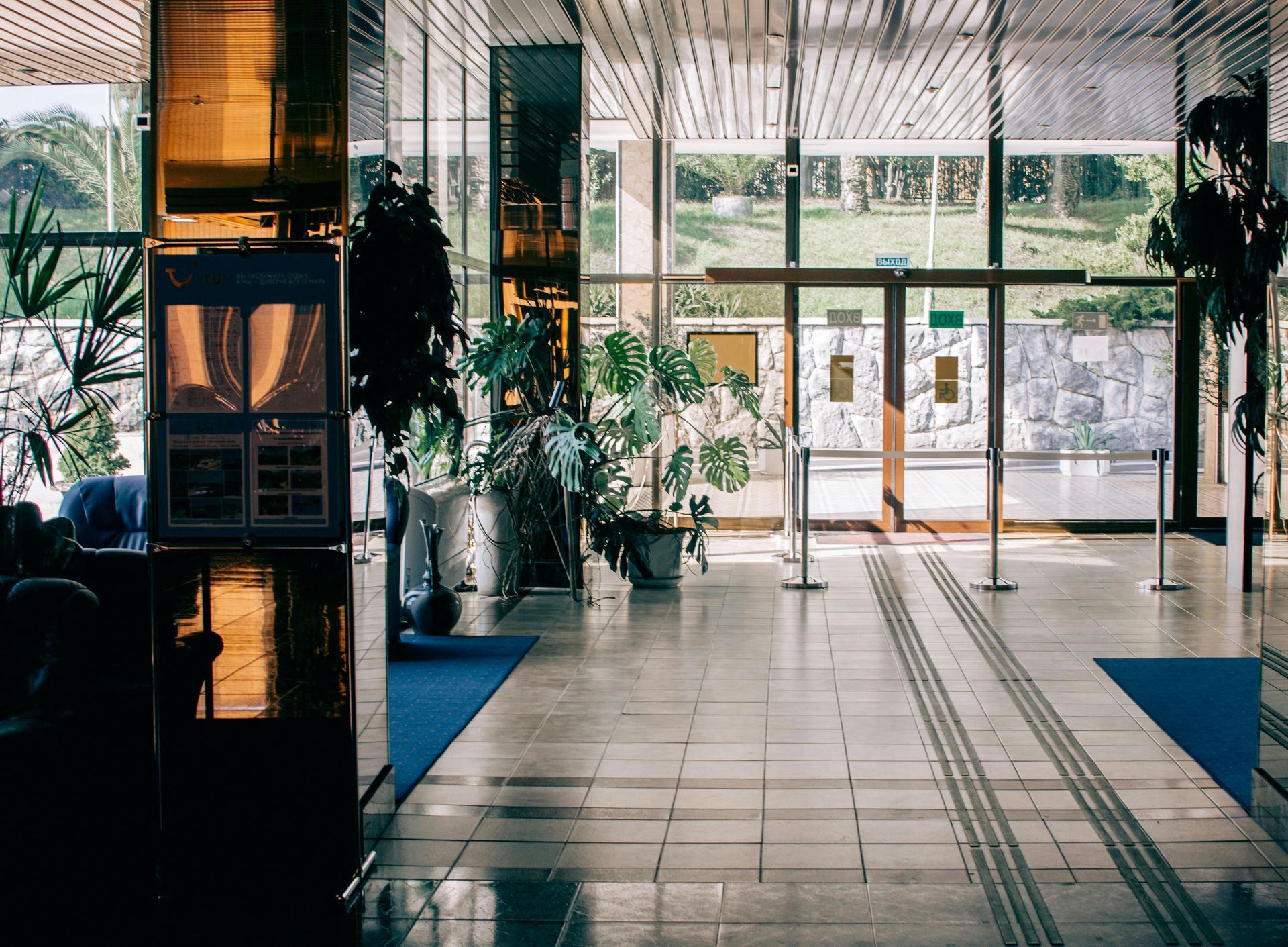 Brightly lit lobby with plants and large windows overlooking a green space.