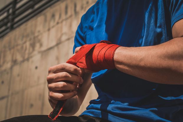 A man is wrapping his wrist with a red bandage.