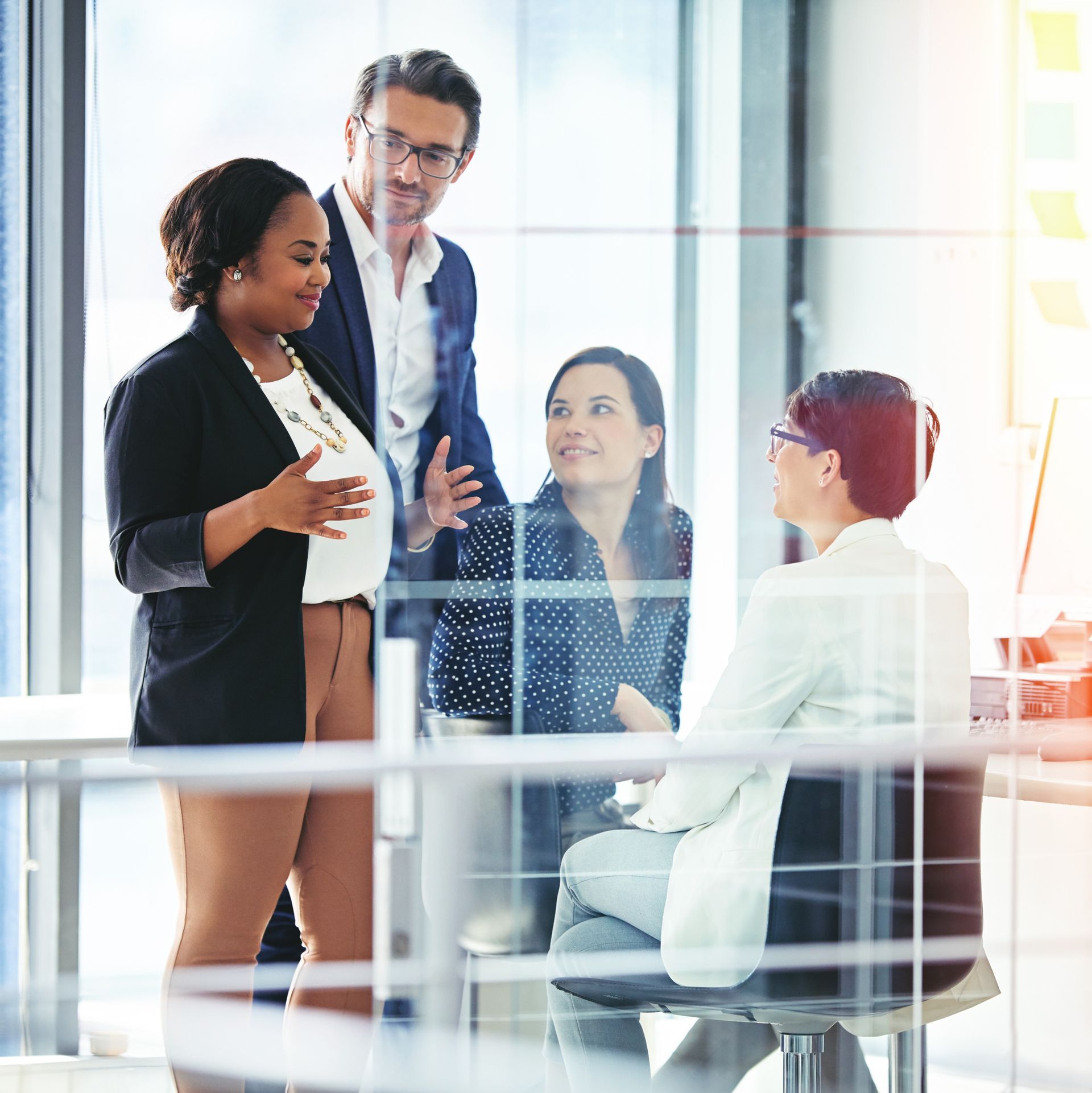 Business team in an office, discussing ideas. Diverse group, smiling. Modern setting, glass walls.