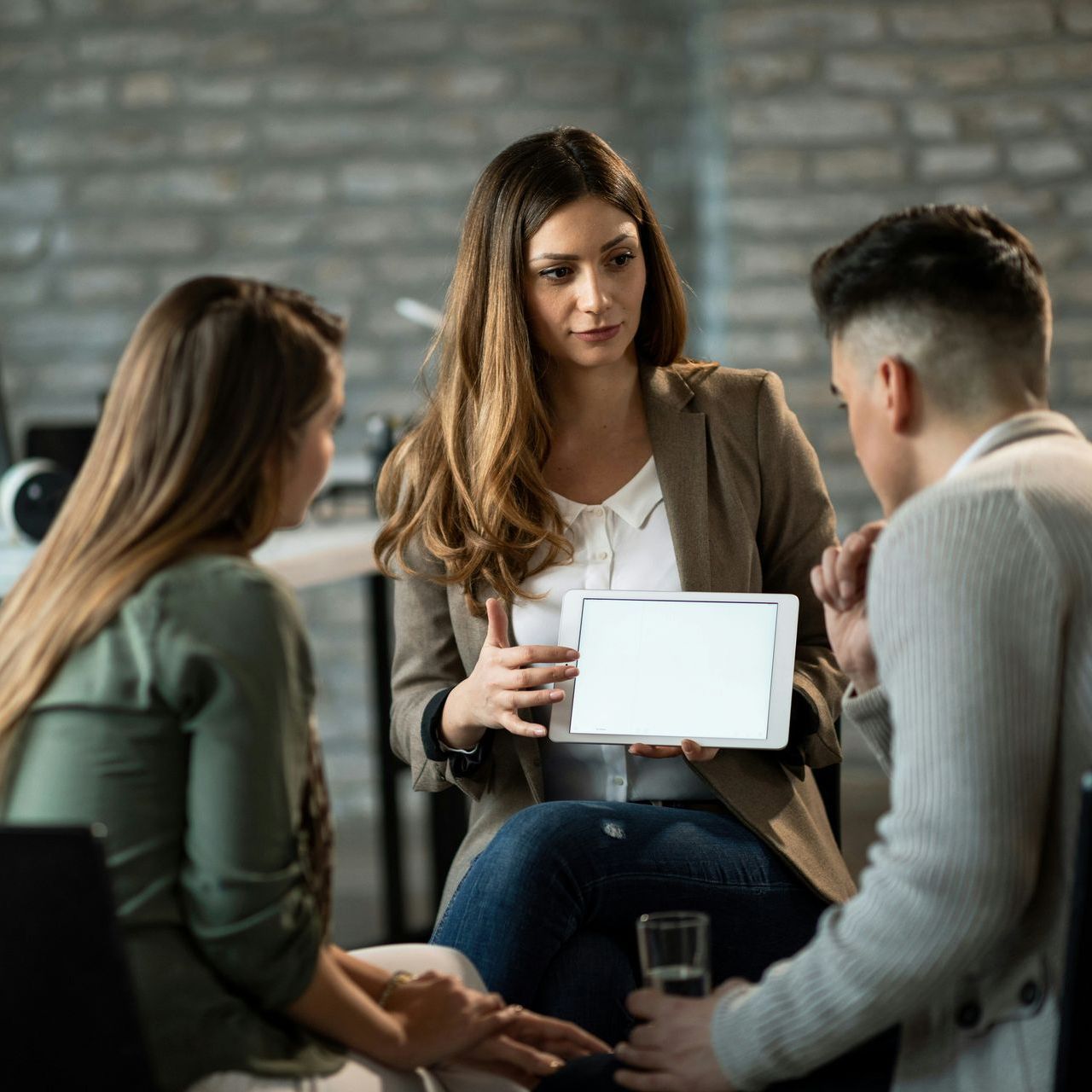 Woman showing tablet to a couple, likely counseling. Office setting, neutral tones.