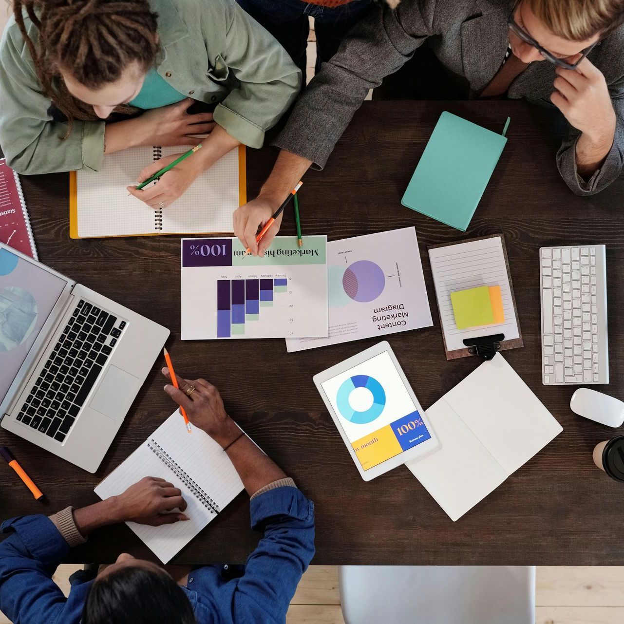 Group of people working around a table with papers, laptop, and tablet, taking notes.