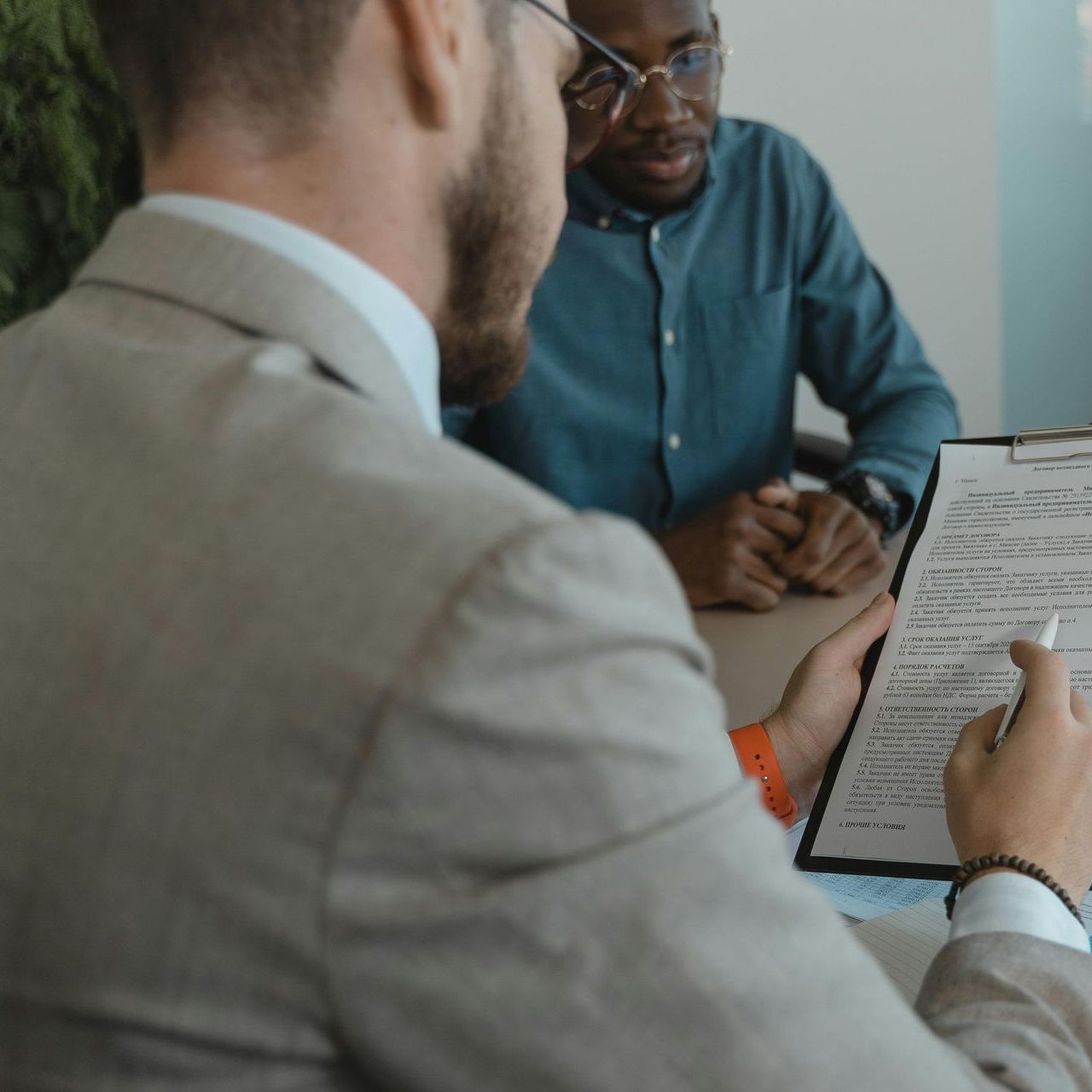 Man in a suit reviews document with a man in blue shirt. Office setting.