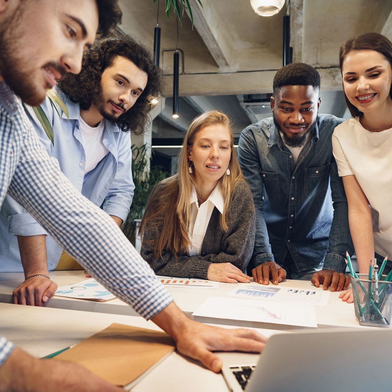 A diverse group of people collaborating around a table, reviewing papers and a laptop in a modern office setting.