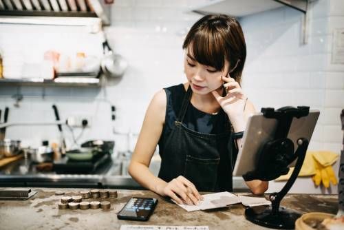 a woman is sitting at a counter in a commercial kitchen (restaurant) calculating bills - small business debt collection
