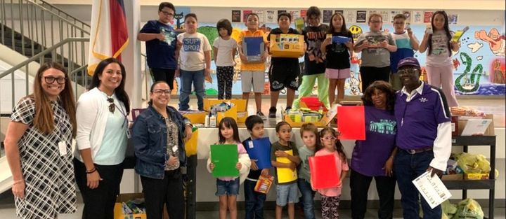 A group of children and adults posing for a picture in a school setting, holding signs and awards.