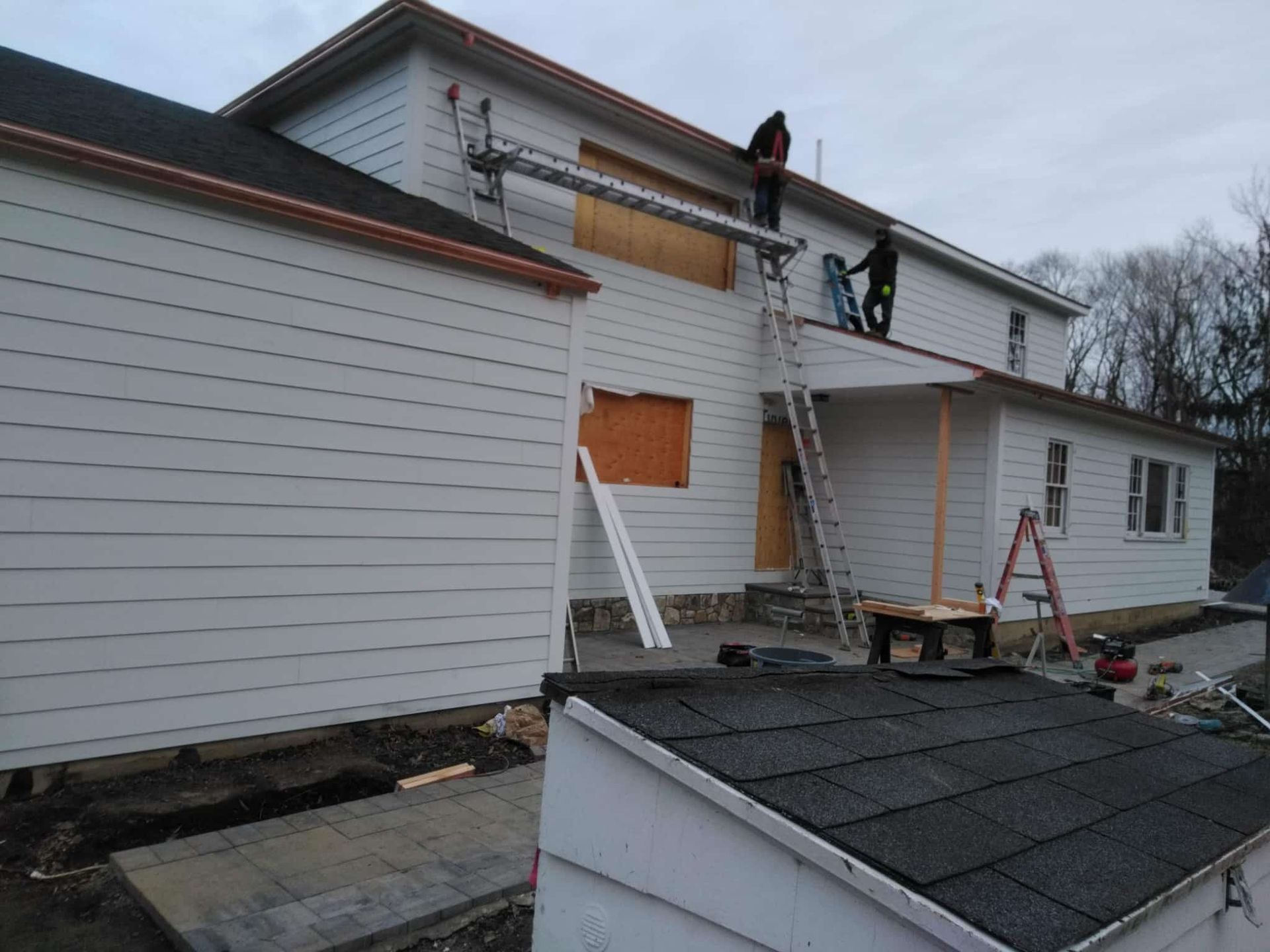 Roofer using a nail gun to install asphalt shingles on a roof on a sunny day.