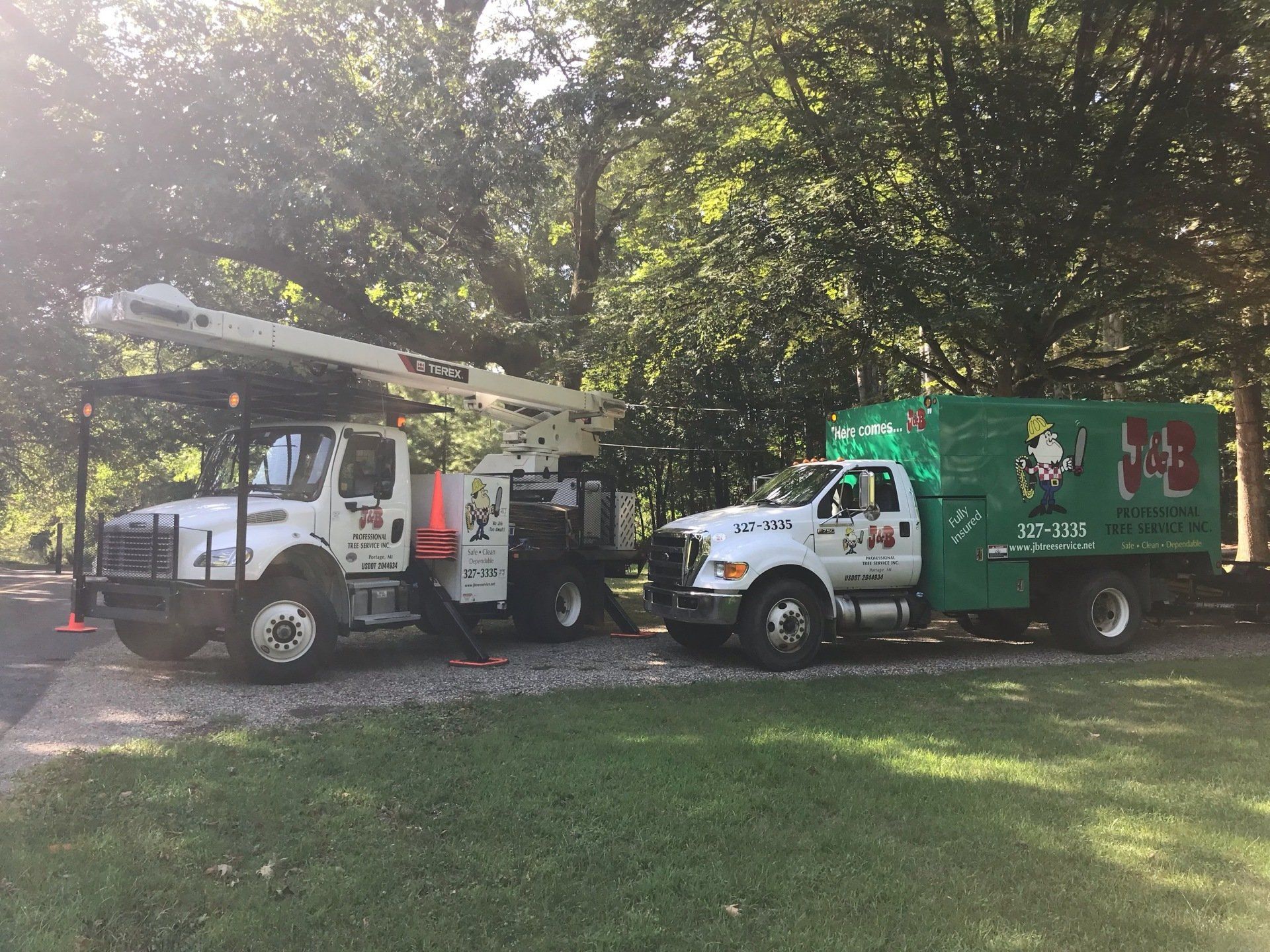 Two white tree service trucks parked on grass, one with a raised crane, near trees.
