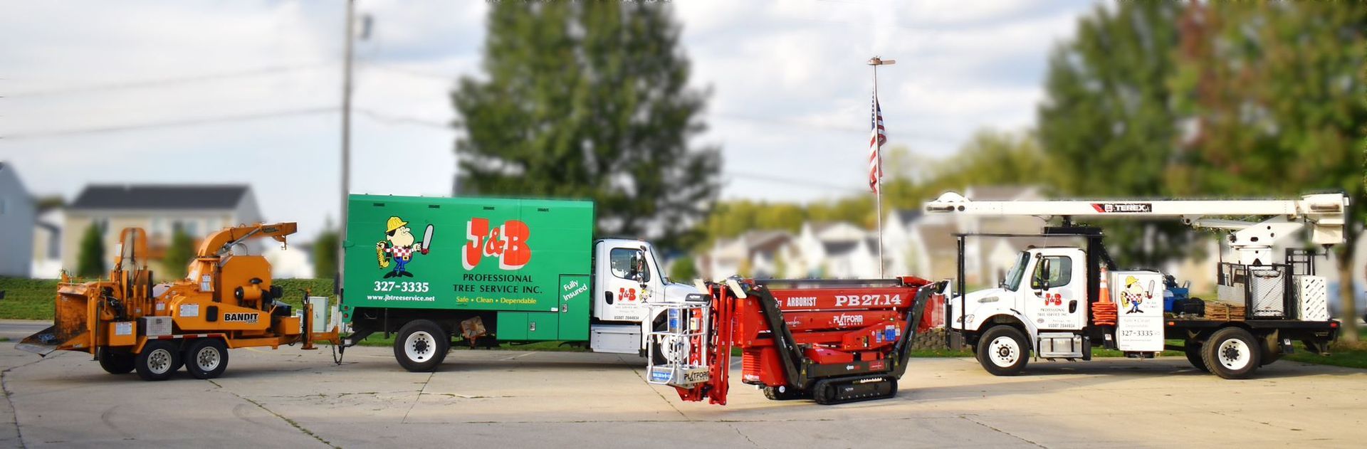 Tree service trucks parked on a street. Includes a wood chipper, green box truck, red truck, and bucket truck.