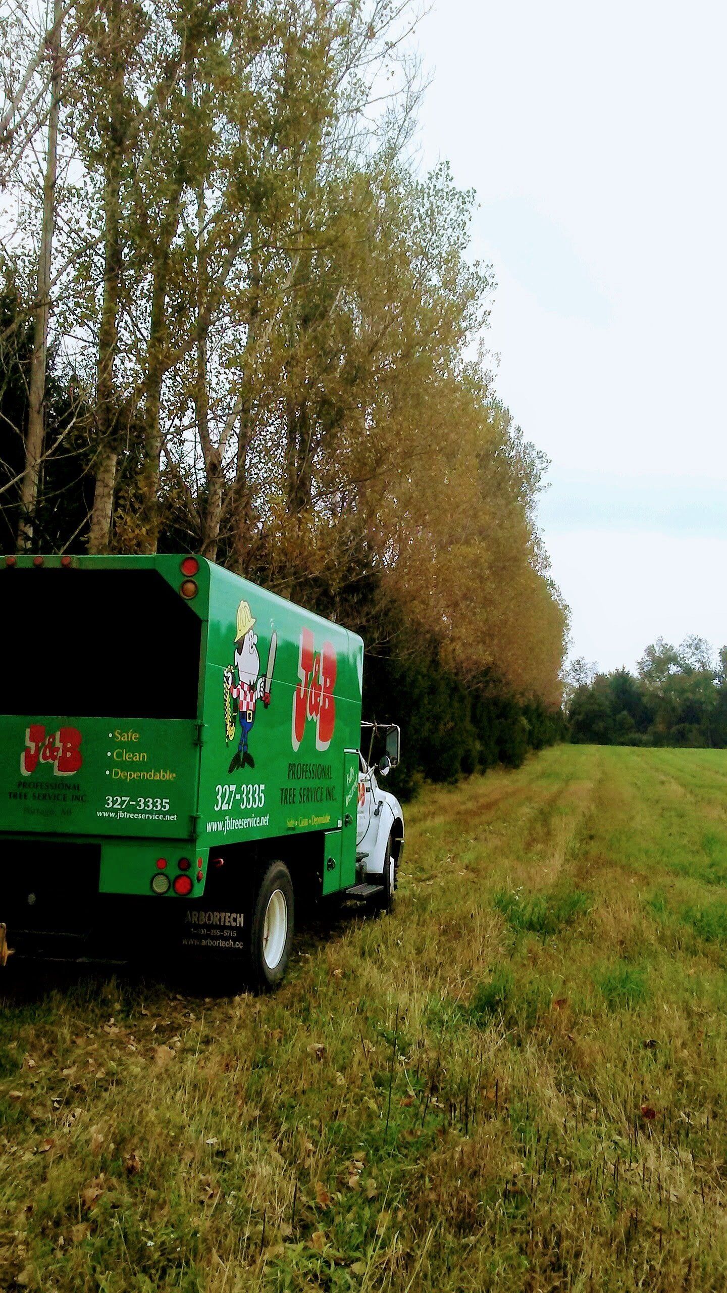 Green truck with logo parked next to a line of trees and a field.
