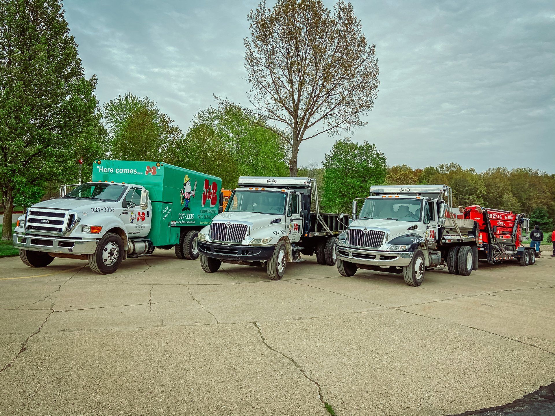 Three work trucks parked outdoors, with the same company logo; cloudy sky.