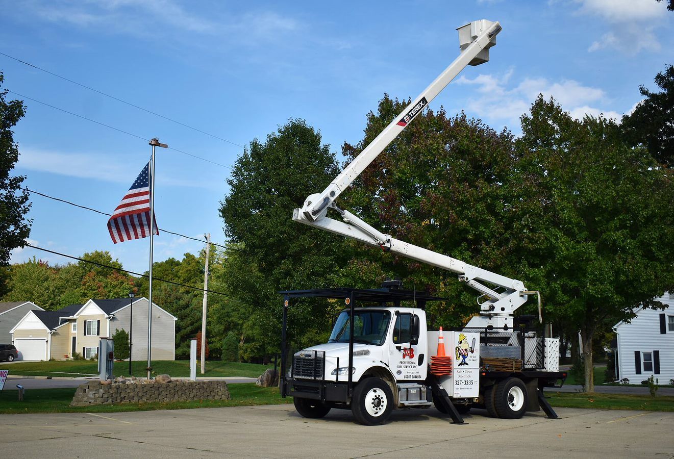 Bucket truck with extended boom near American flag and residential area.