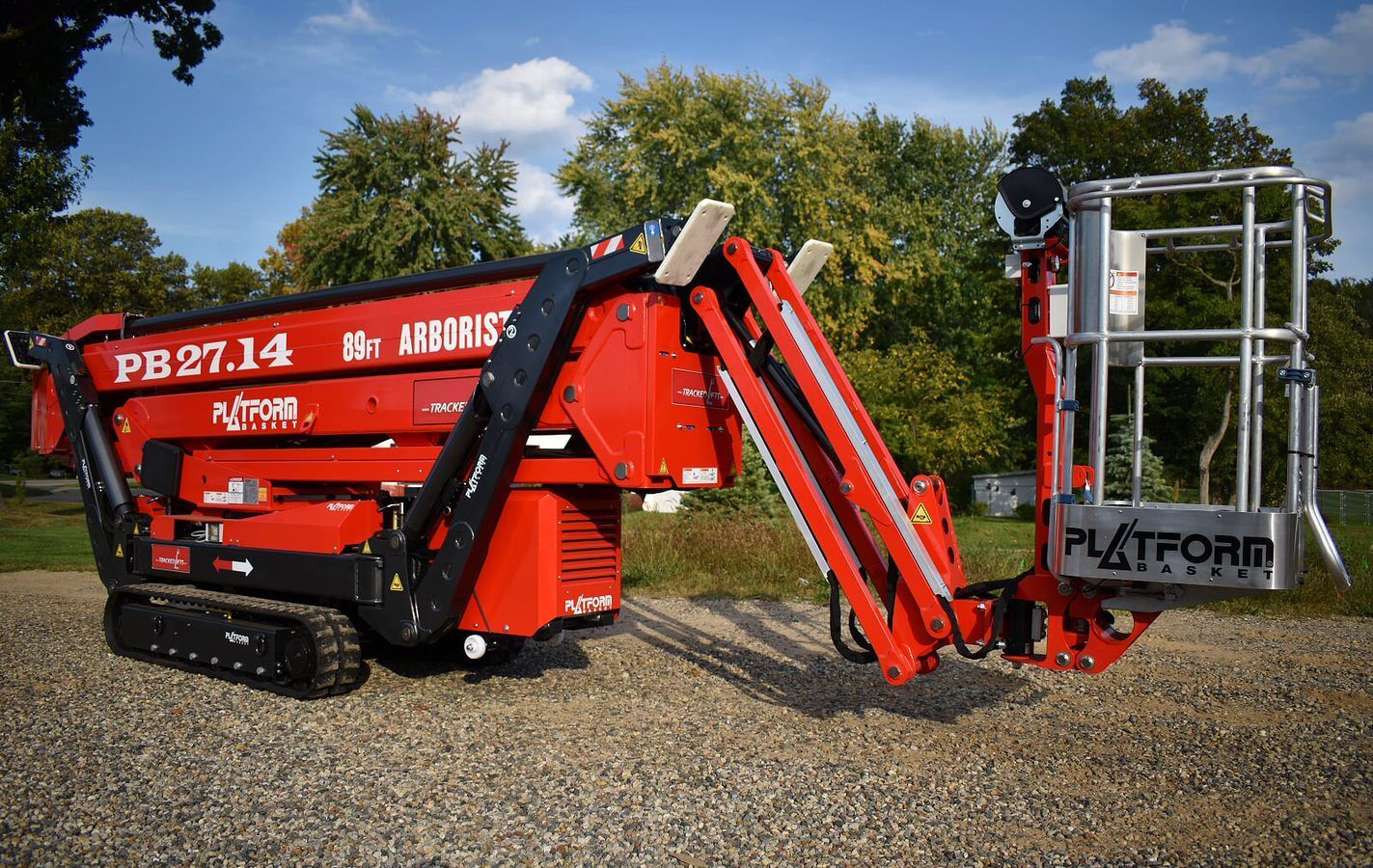 Red tracked aerial lift, extended boom, holding a platform in an outdoor setting.