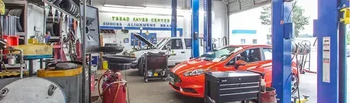 A red car is sitting on a lift in a garage. | TNT Tire Point S Auto Service