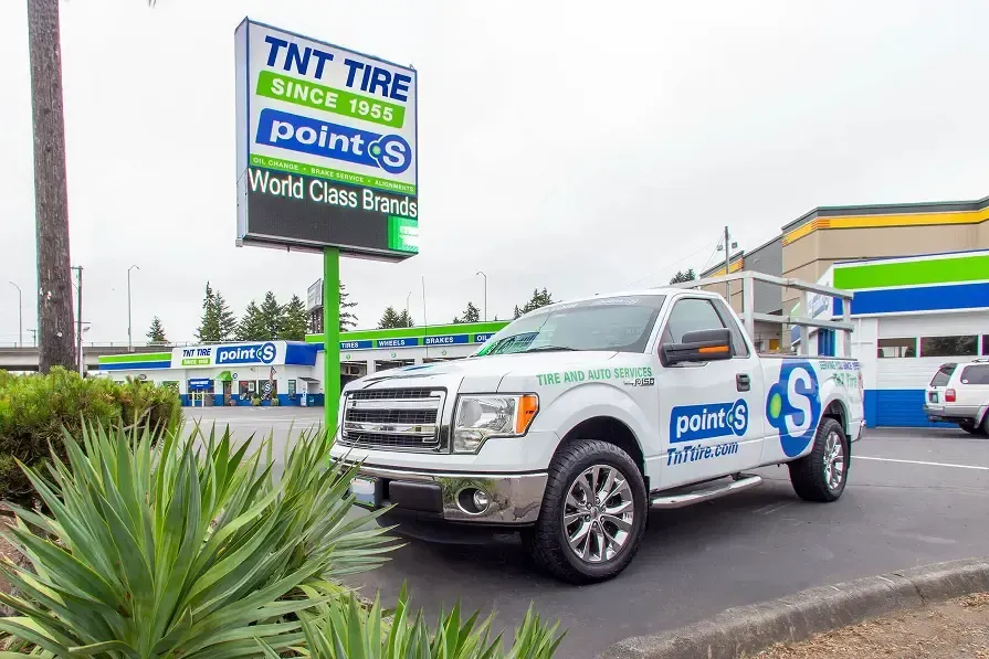 A truck is parked in front of a sign that says tat tire | TNT Tire Point S Auto Service