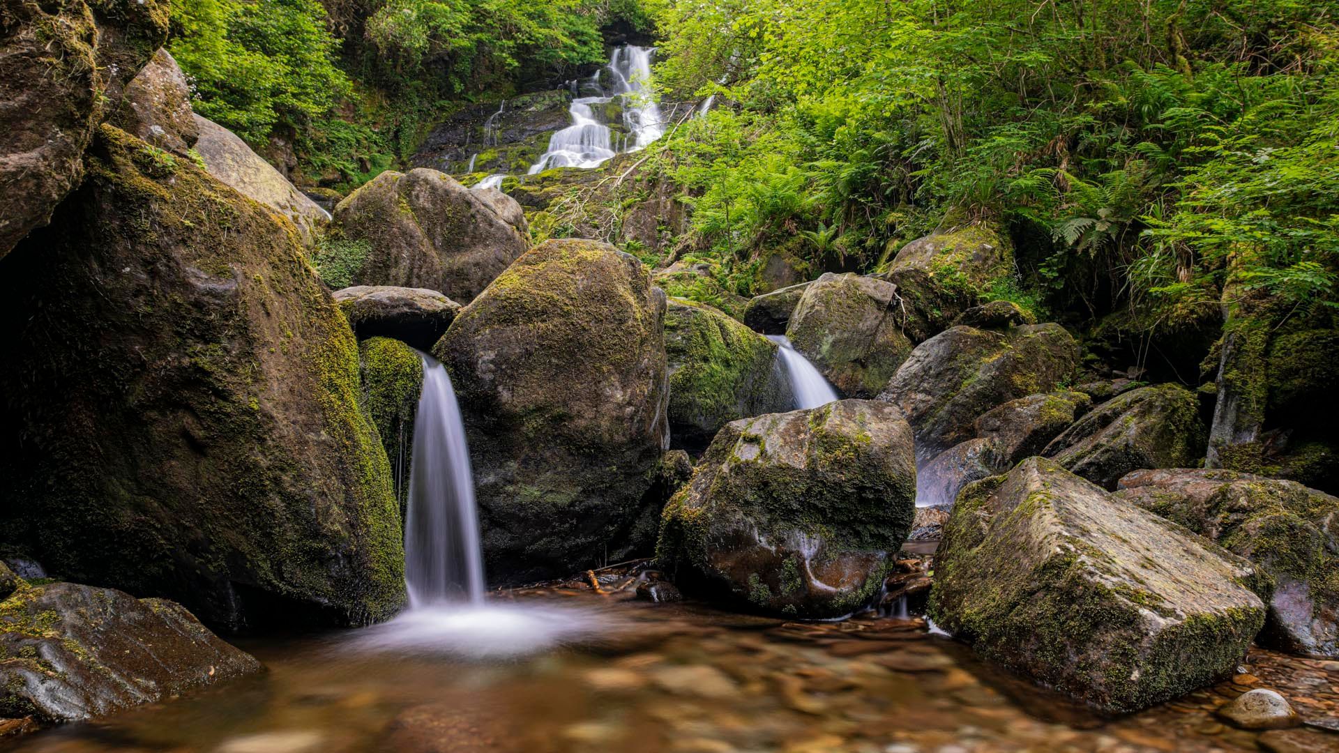 A small waterfall is surrounded by rocks in the middle of a forest.