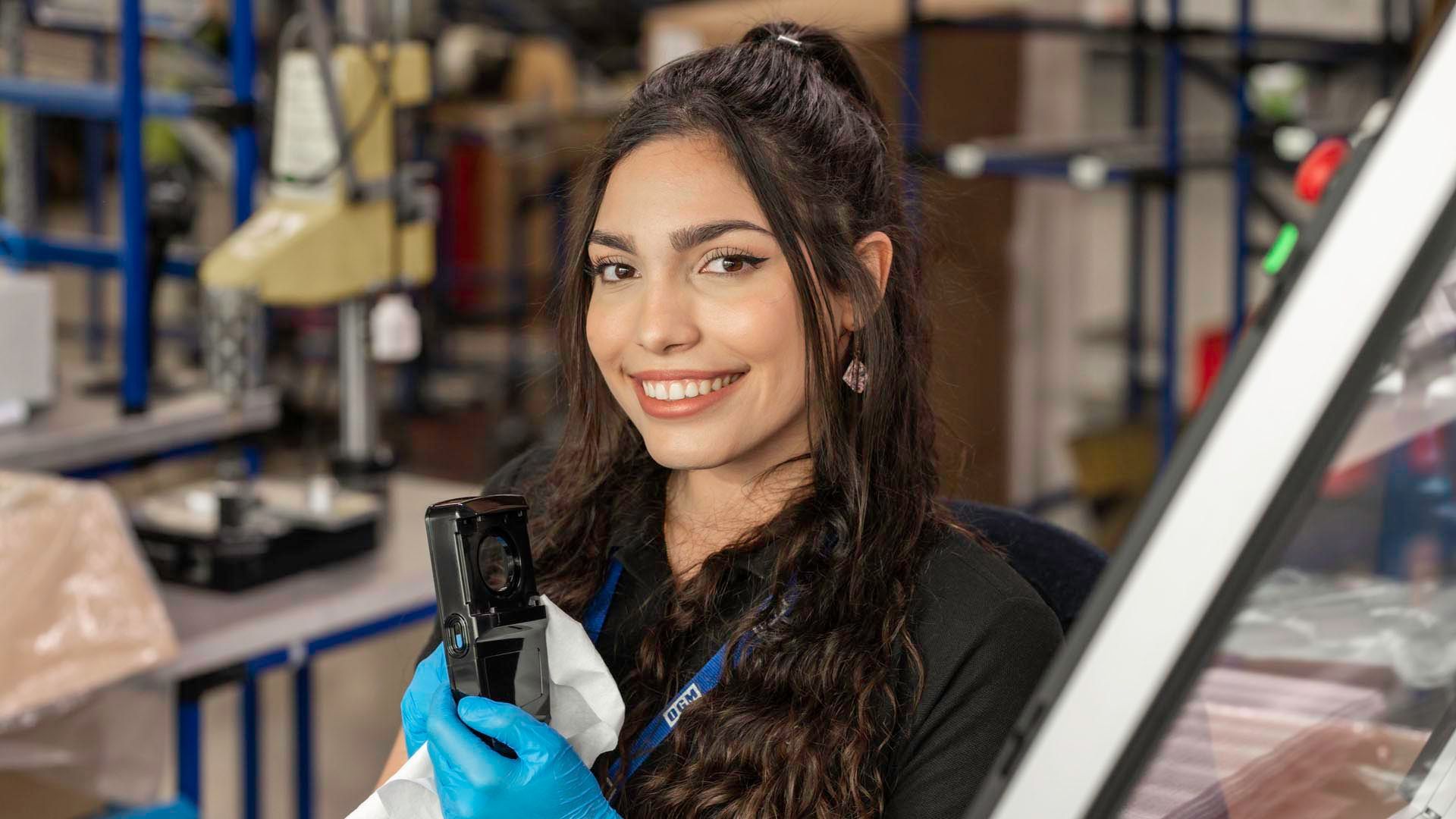 a woman is holding a plastic object in a factory and smiling .
