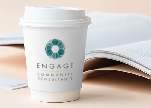 a coffee cup with the word engage community consultants on it is sitting next to an open book .