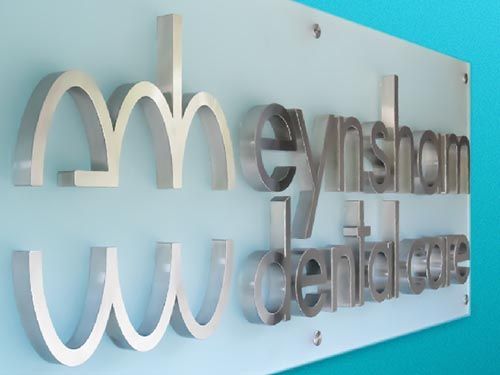 a stainless steel sign for a dental care company is hanging on a blue wall.